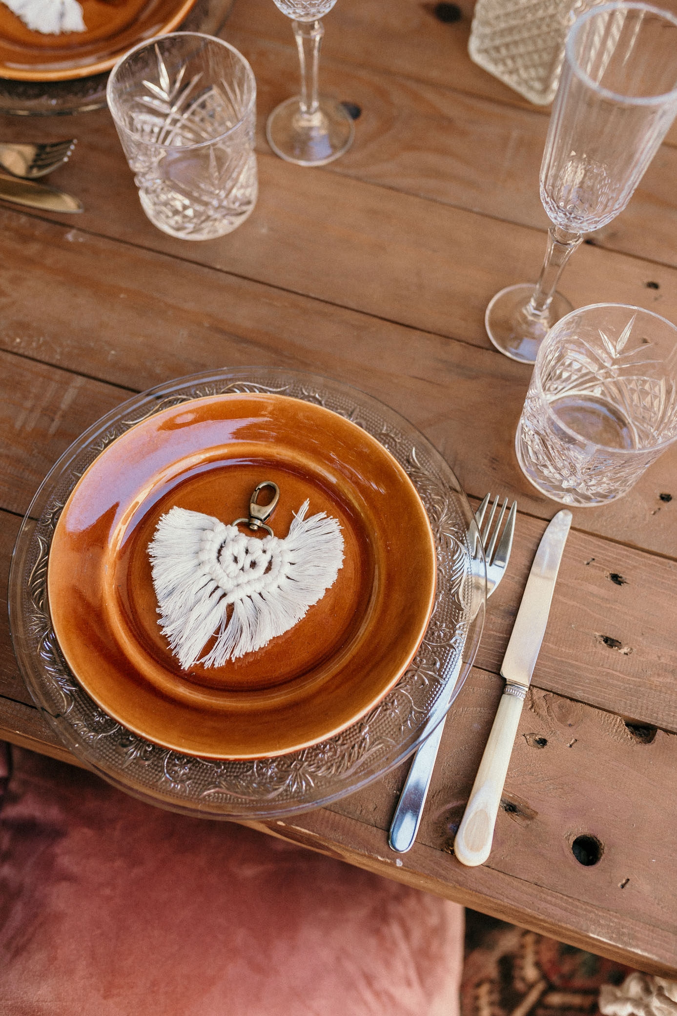 table basse bois, assiettes orange porcelaine, porte-clés macramé, couverts, verre cristal, pouf orange, inspiration bohème, mariage bohème