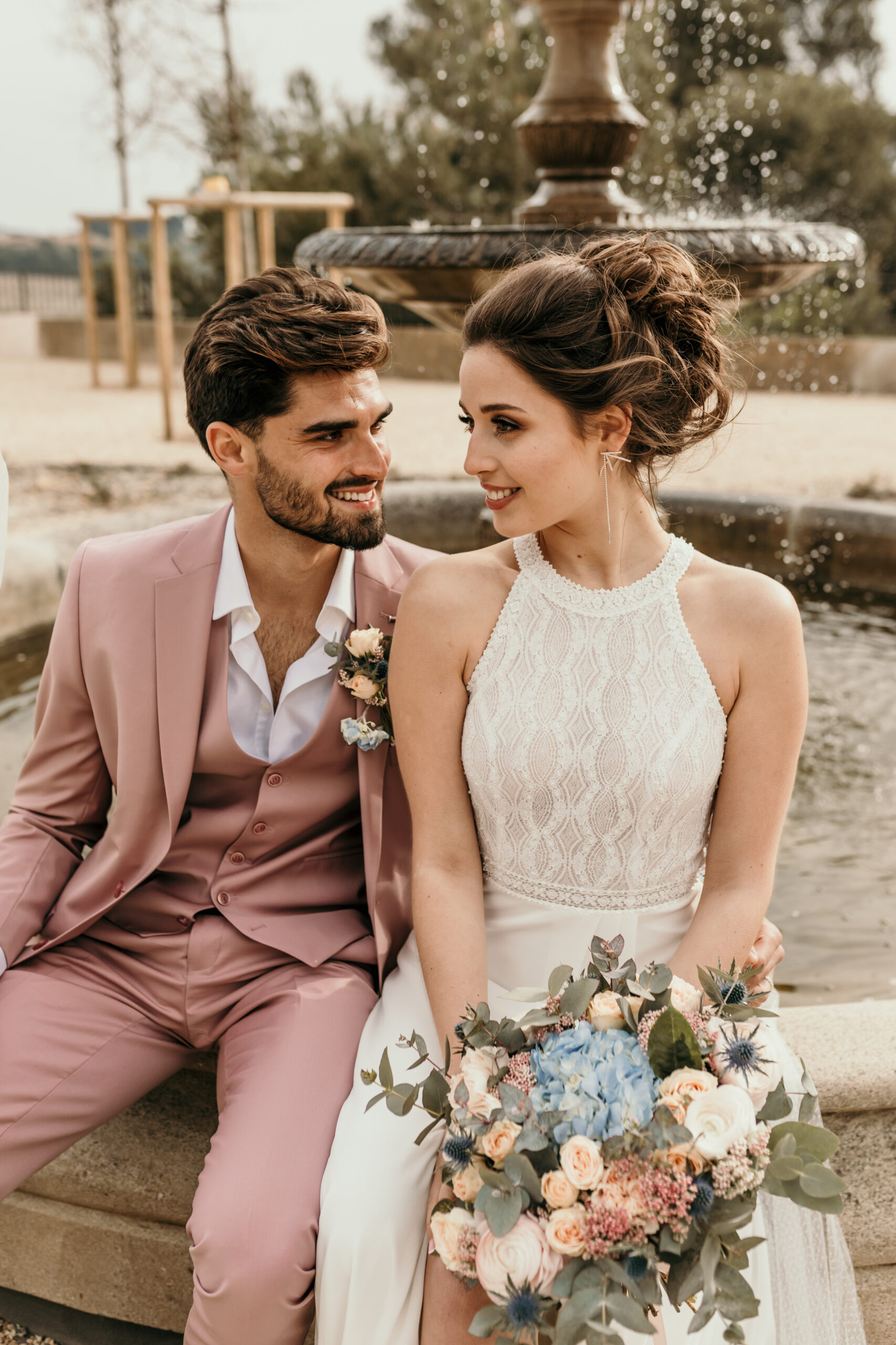 couple de mariés, fontaine, bouquet de mariée, robe de mariée bohème chic, costume de marié rose, chignon de mariée, Château Capitoul mariage
